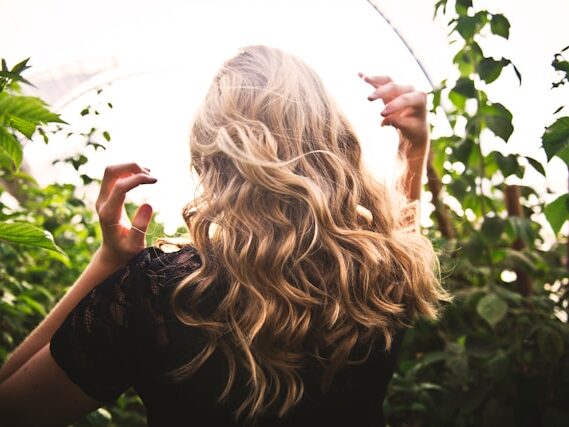 周りに植物が咲いていて、ロングヘアーの女性の後姿の画像