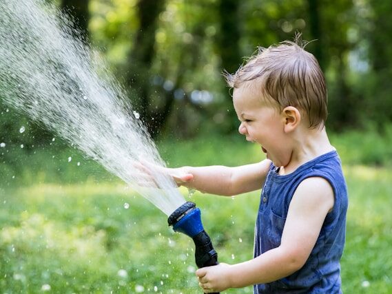 外国の男の子が、ホースの水を思いっきり出して叫んだ顔をしている画像