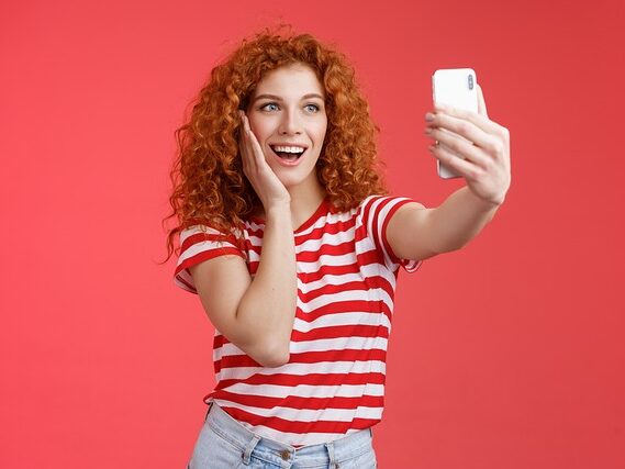 赤と白のボーダーの服を着たカーリーヘアーの女性が自撮りして笑っている画像