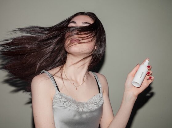 長い髪の女性が、ミニスプレーを片手で持っていて、髪で目が隠れている画像