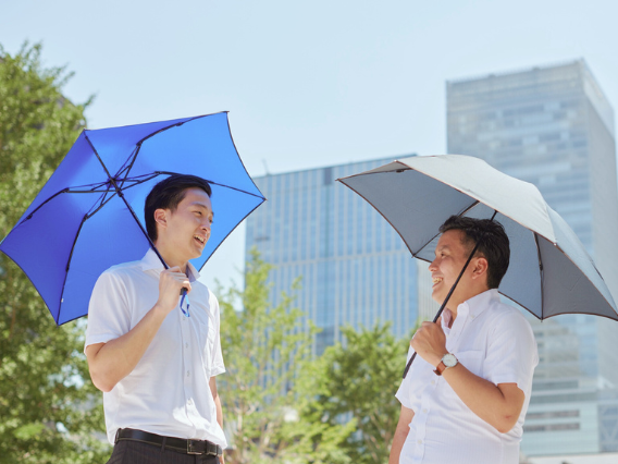 スーツ姿の男性二人が日傘を指して向き合っている画像
