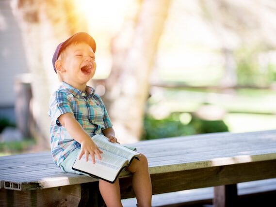 子どもがベンチに座って本を読みながら笑っている画像
