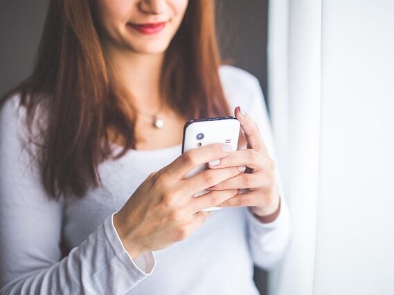 髪の長い女性が両手で携帯電話をもって見ている画像