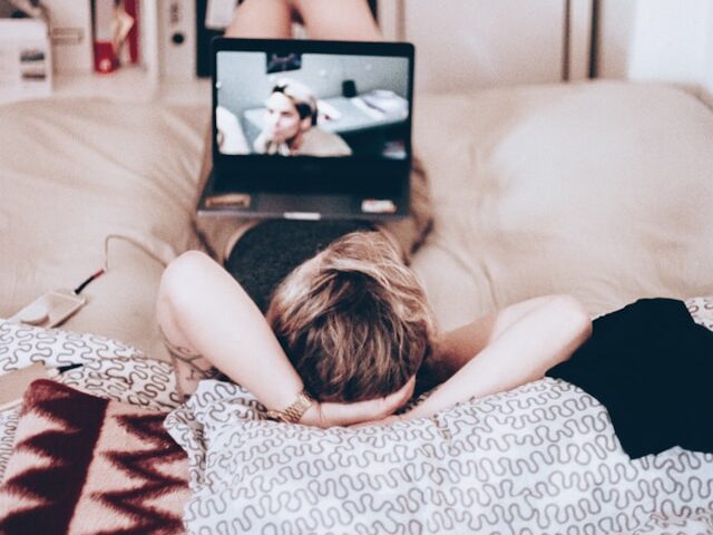 女性が寝転がって、膝の上のパソコンの映像を観ている画像