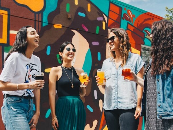 おしゃれな女性4人が、外でビールを持って笑っている画像