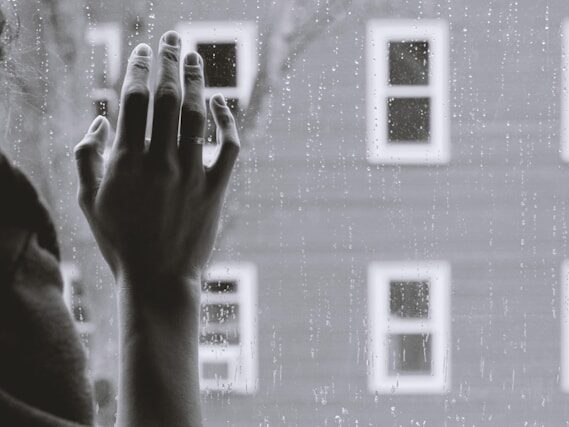 雨の日に室内から窓に手を当てている画像