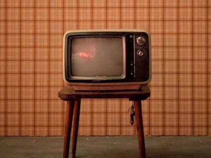 背景がチェック柄で、古いテレビが小さい台の上に置いてある画像