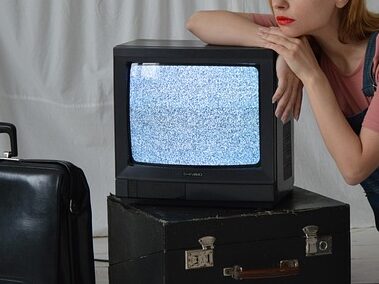 女性が砂嵐のテレビにもたれかかっている画像