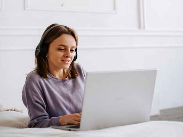女性がヘッドフィンをしながらパソコンを観ている画像