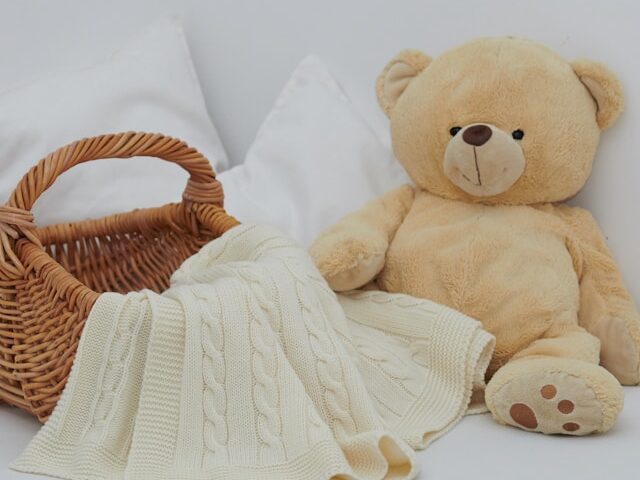 大きなクマのぬいぐるみとかごとニットが置いてある画像
