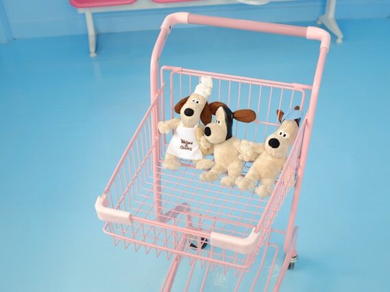 ピンクのショッピングカートにイヌのぬいぐるみが三体乗っている画像