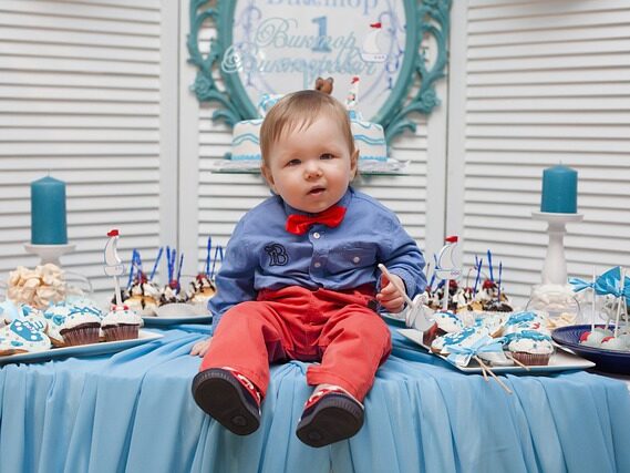男の子がテーブルの上に座って、1歳の誕生日を祝っている画像