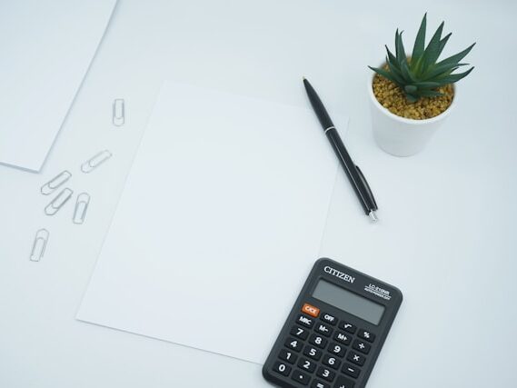 テーブルに紙、電卓。クリップ、観葉植物が置いてある画像