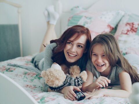 母と娘がベットに寝そべってテレビを観ている画像