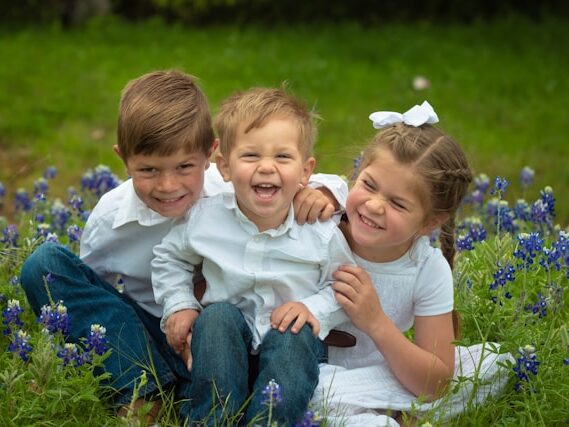 芝生で子ども3人が座って笑っている画像