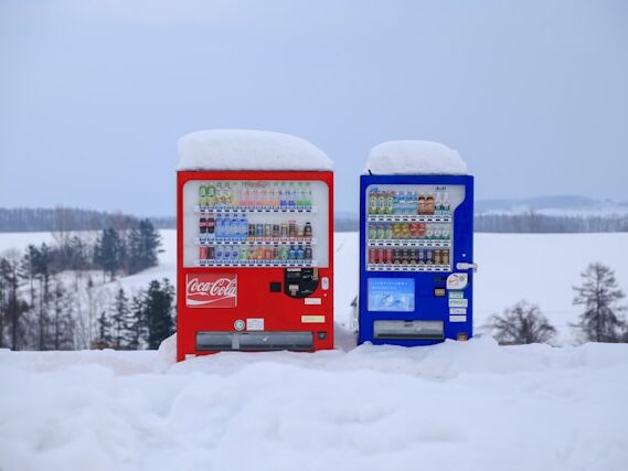雪の中に並んだ赤と青の自動販売機の画像