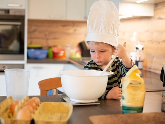 シェフ帽をかぶった男の子が料理している画像