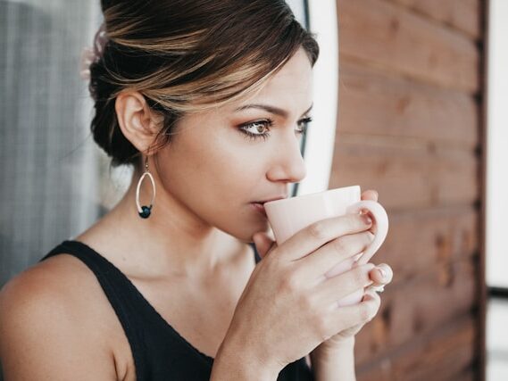 女性が壁に寄りかかってコーヒーを飲んでいる画像