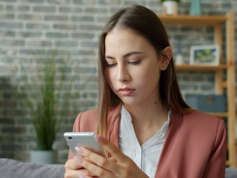 髪の長い女性が両手で携帯電話をもって見ている画像