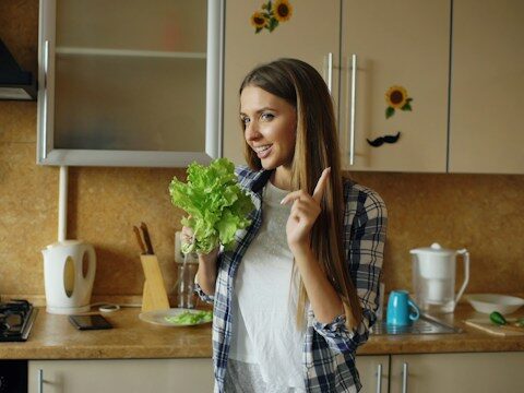 キッチンで女性が葉物野菜を持っている画像