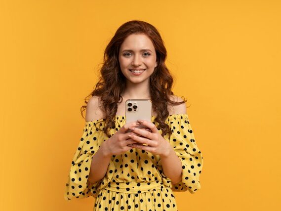 黄色い服を着た女性が両手で携帯を持っている画像
